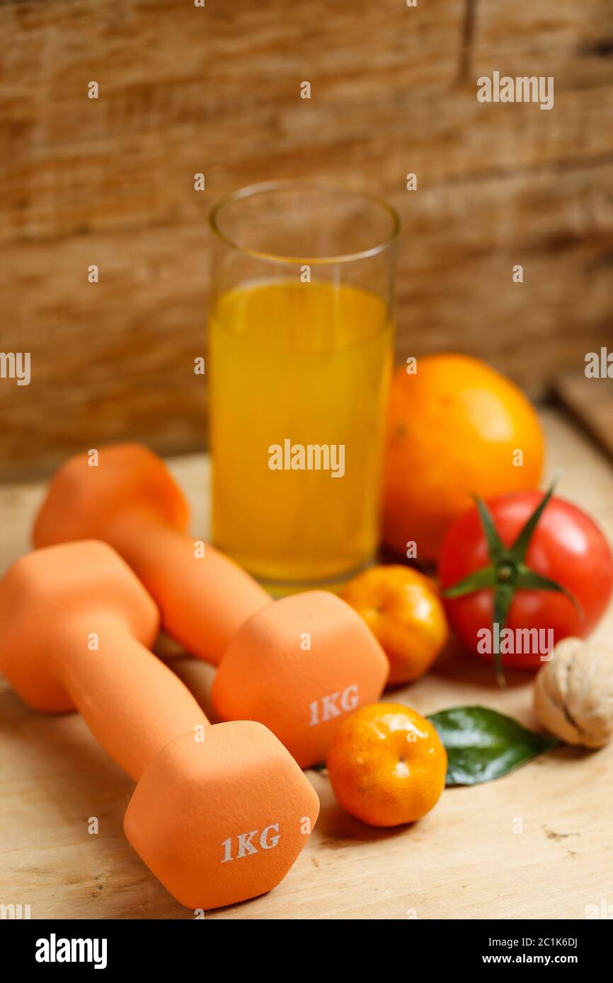 Dumbbell, orange juice, fruit and nuts on the wooden table, sport and