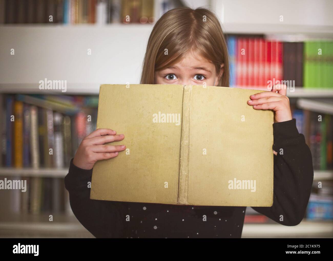 Cute little schoolgirl holding book and smiling at camera Stock Photo ...