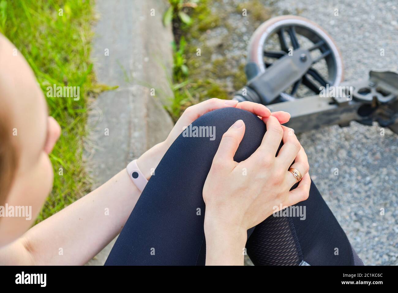 The girl hurt her knee and holds her hands behind her leg after riding
