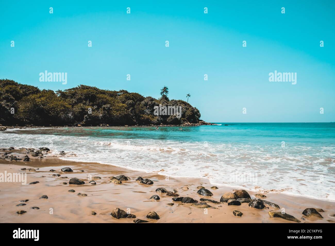 Beautiful secluded beach on an isolated island. Blue water and white waves spume on a sandy beach with stones in Sri Lanka. Escape to remote island Stock Photo