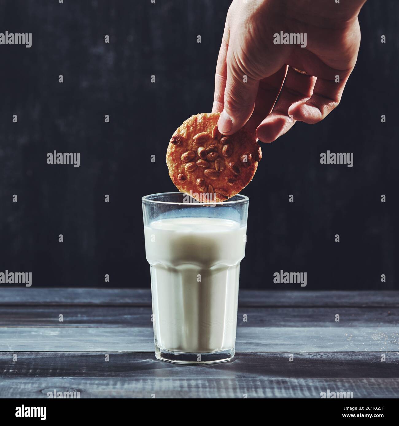 Womans hand dunking a homemade cookie in a glass of milk over a black ...