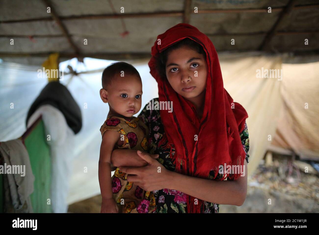 A Rohingya mother with her child stands in front of a makeshift camp at Kutupalong refugee camp, Bangladesh, Tuesday, Oct. 03, 2017. Stock Photo