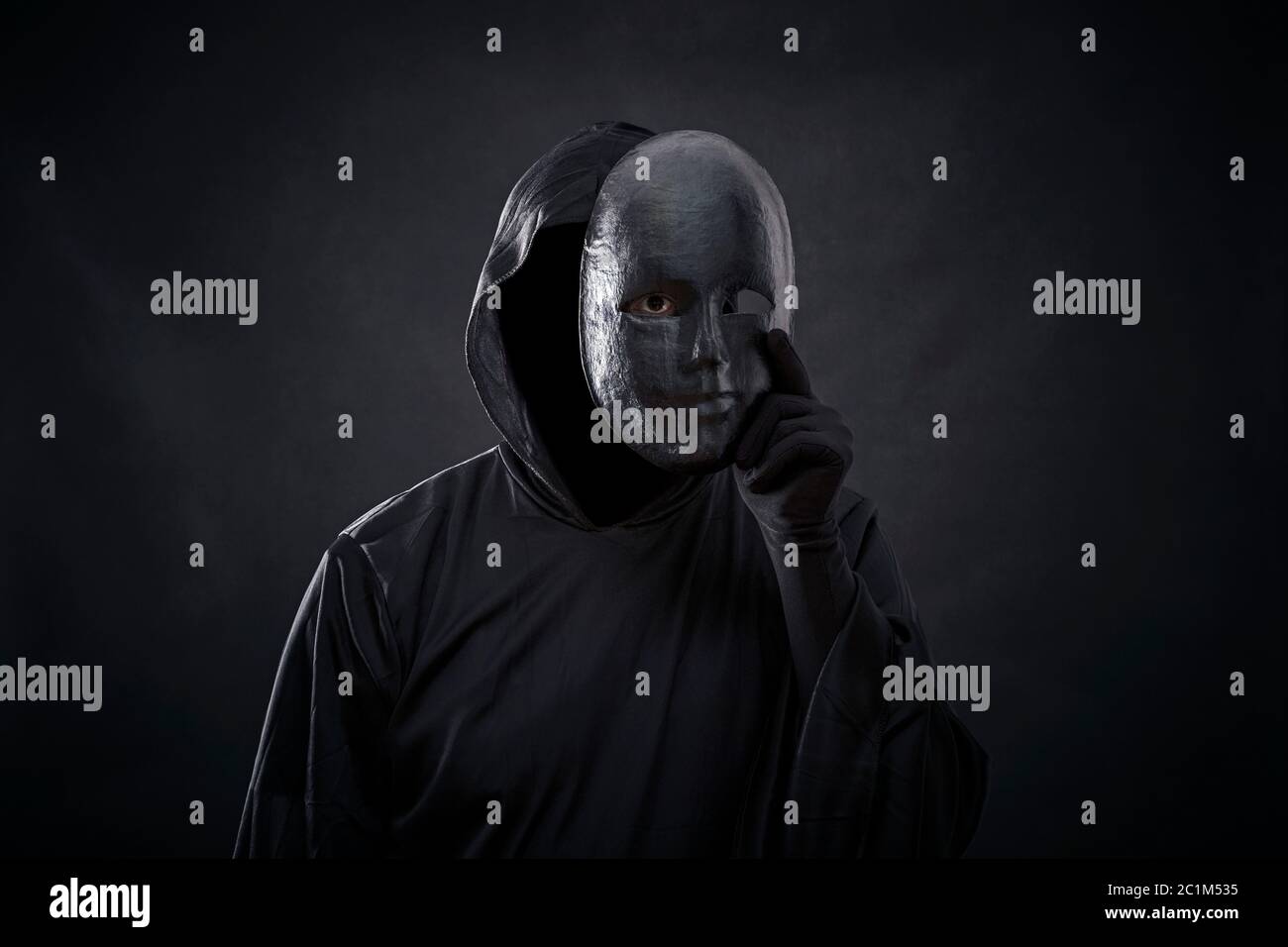 Scary figure in hooded cloak with mask in hand Stock Photo