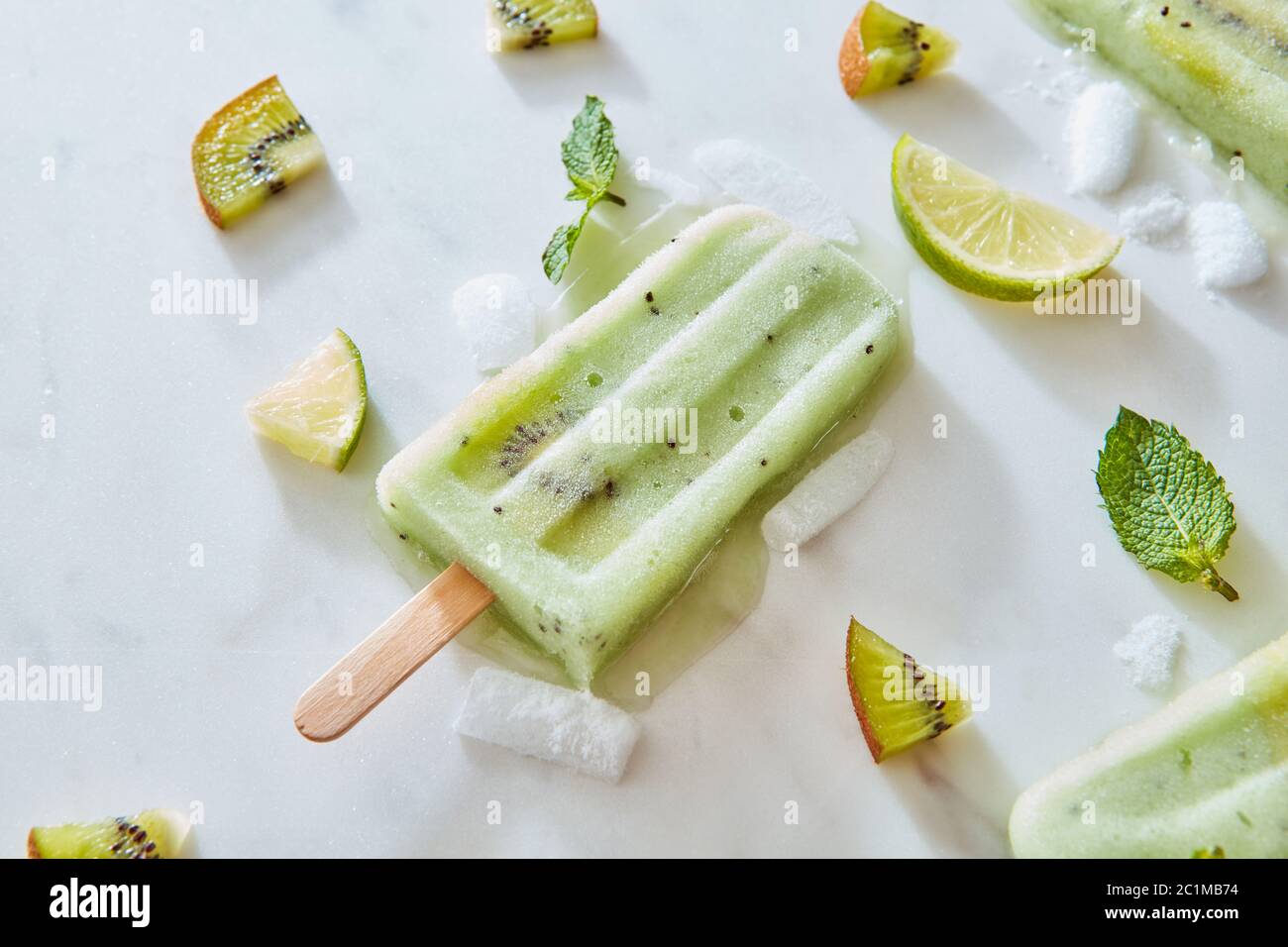 Frozen fruit juice on a stick with a piece of fresh kiwi on a gray marble background with mint