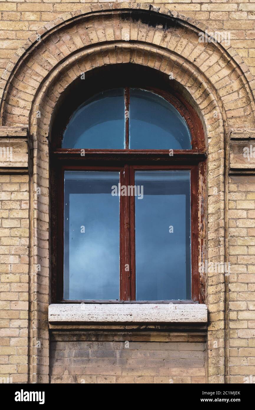 Vintage arched window in the wall of yellow brick. Black glass in a maroon dark red wooden frame. The concept of antique vintage Stock Photo
