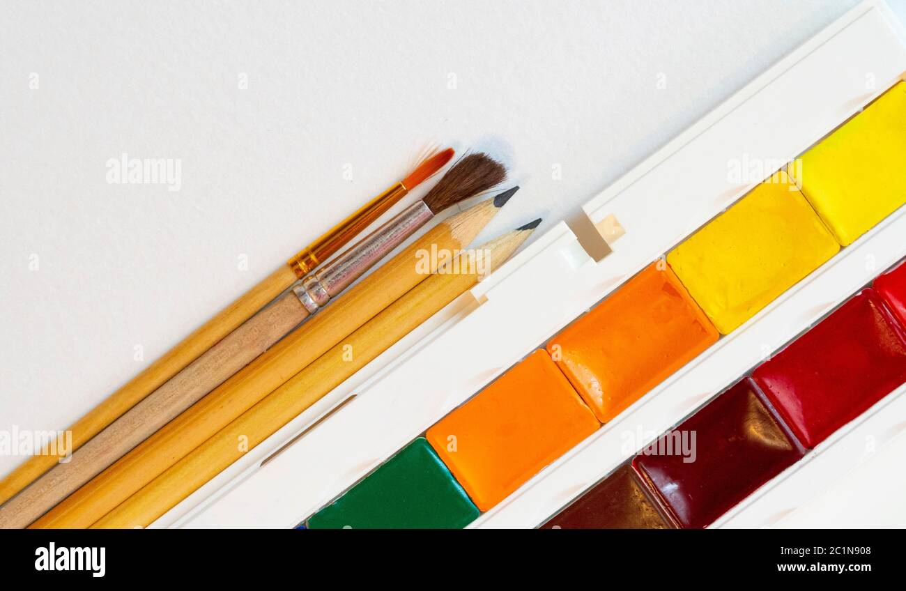 brushes and pencils next to watercolors on white paper top view copy space Stock Photo