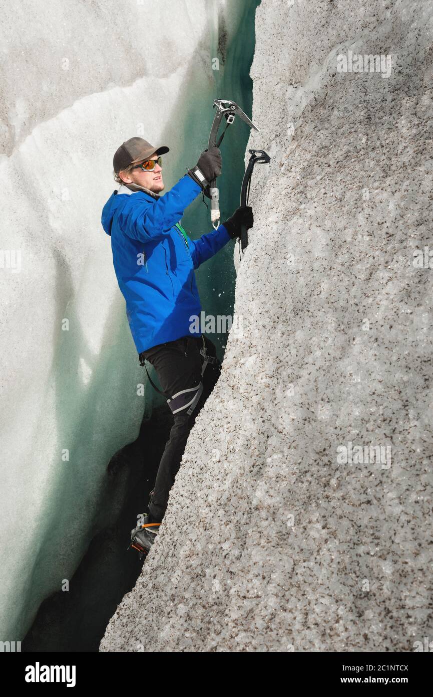 A free climber without insurance with two ice axes rises from a crack in the glacier. Free climbing without ropes Stock Photo
