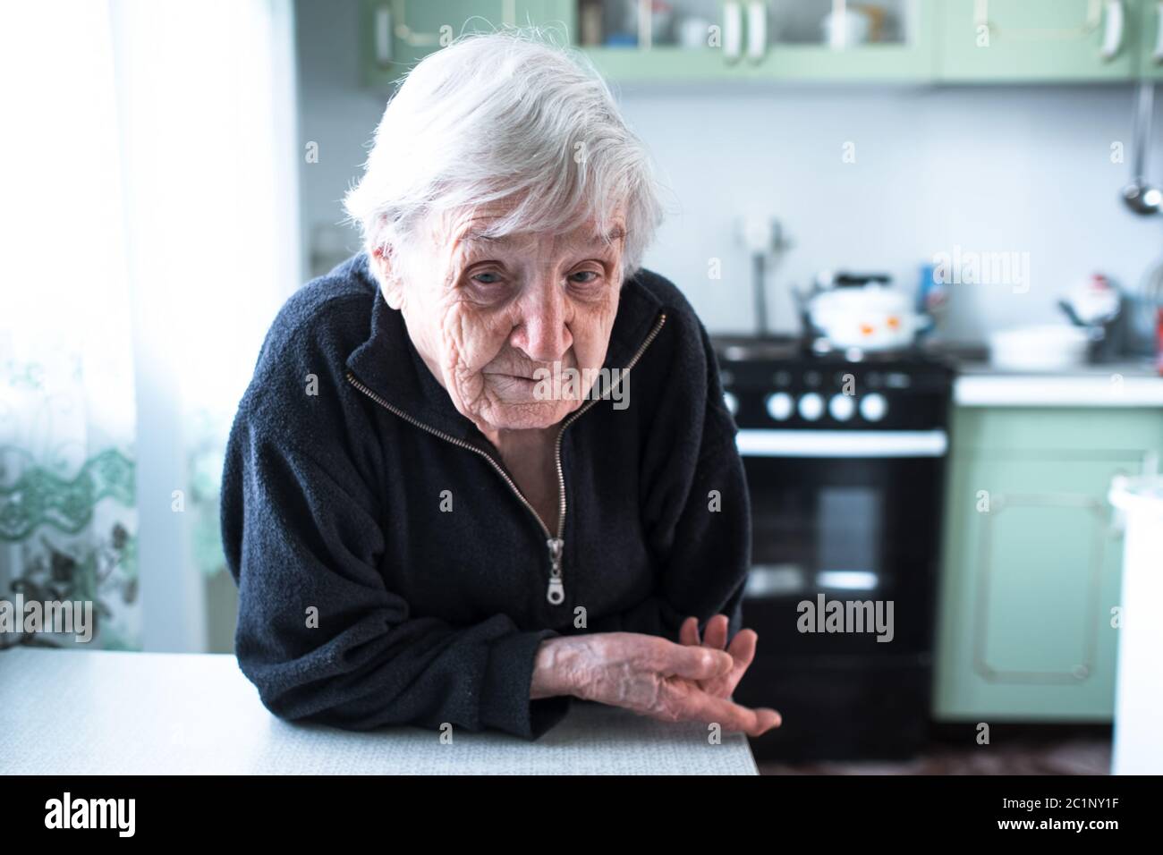 Frustrated gray-haired old woman in her home at the table. Stock Photo