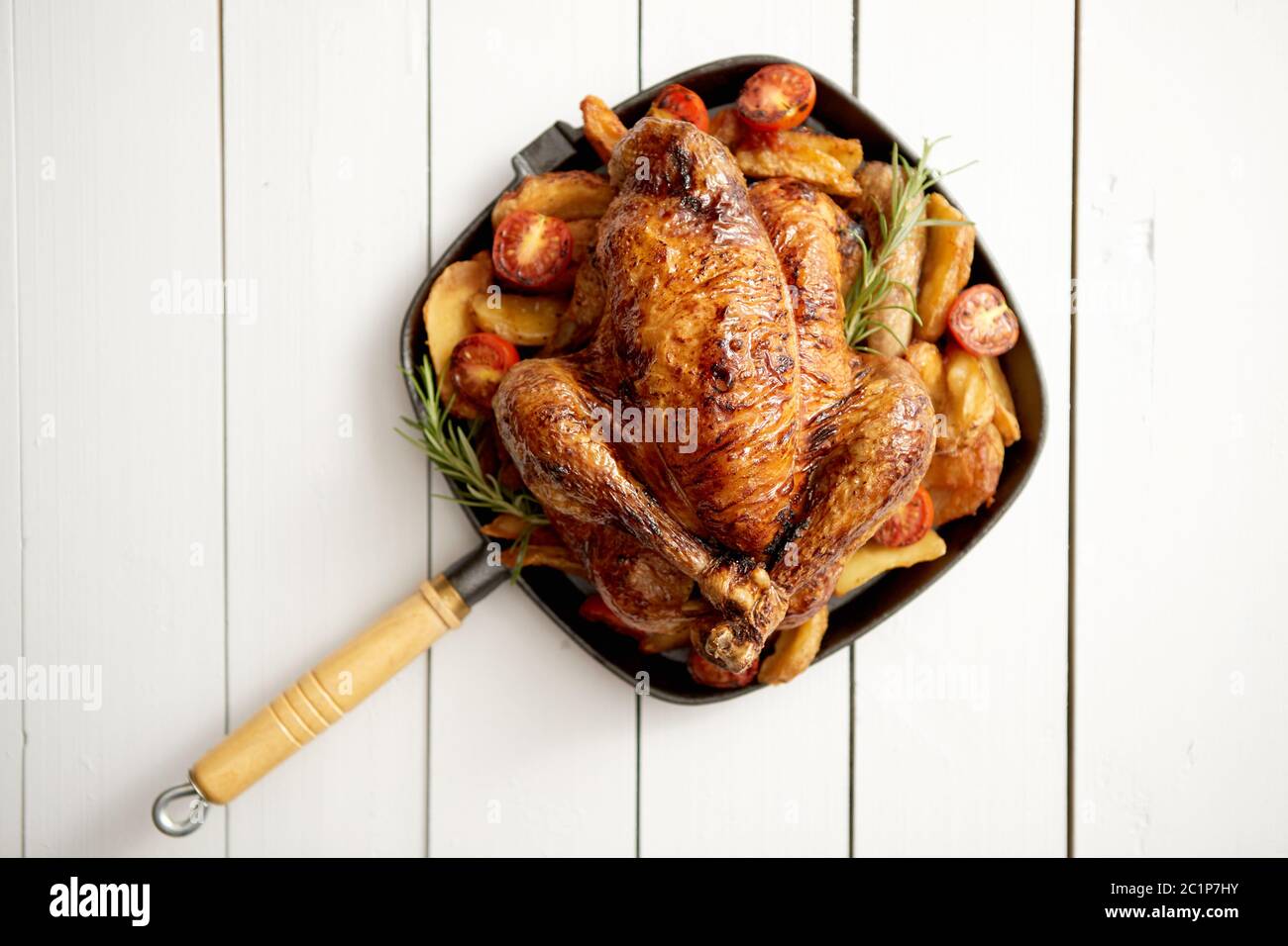 Grilled whole chicken in cast iron black pan with potatoes, tomatos and