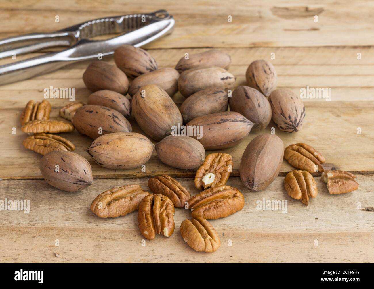 Pecan nuts on rustic wooden table, whole and peeled with nut cracker in background - selective focus Stock Photo