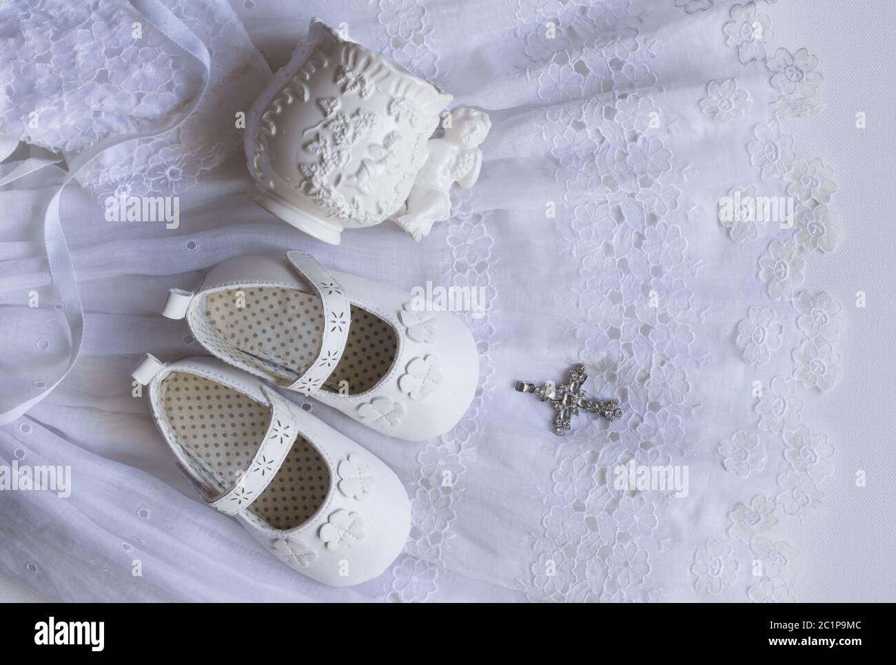 Christening baby shoes, christening cup and crystal cross pendant on vintage lace baptism dress on w Stock Photo
