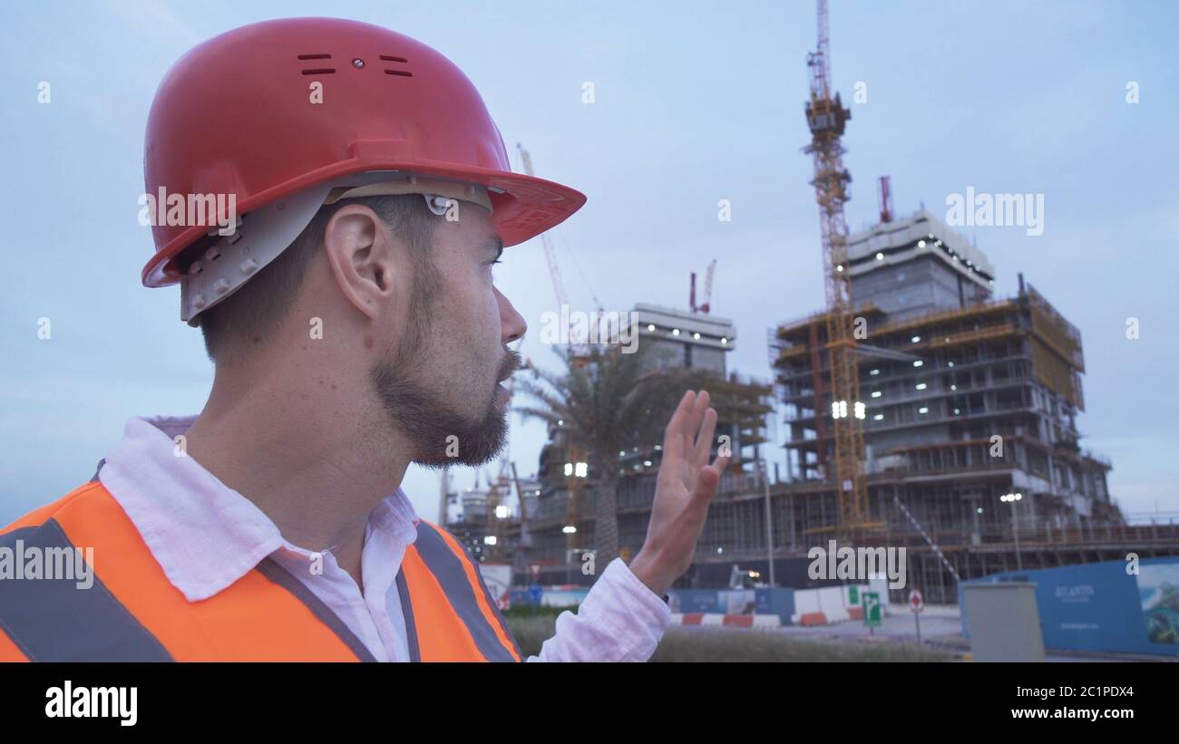 Man in a helmet, architect, engineer, manager tells about the progress of construction in evening Stock Photo