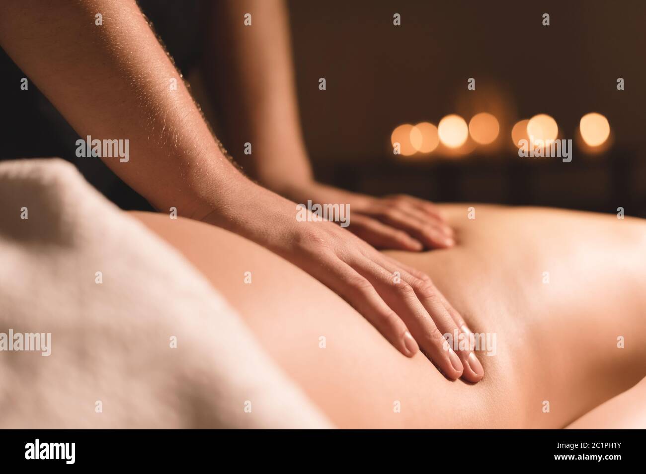 Close-up male hands doing healing massage with oil to a young girl in a dark cosmetology office. Dark key Stock Photo