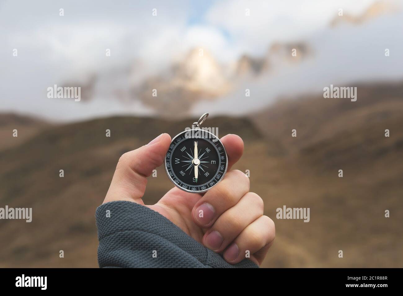A male Hiker is looking for a direction with a magnetic compass in the mountains in the fall. Point of view shot. Man's hand wit Stock Photo