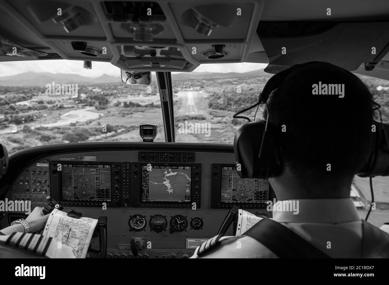 SEP 22, 2011 Pai, Thailand. Pilots in the cockpit during a flight with commercial airplane. Landing with runway scene in valley. Black and white Stock Photo