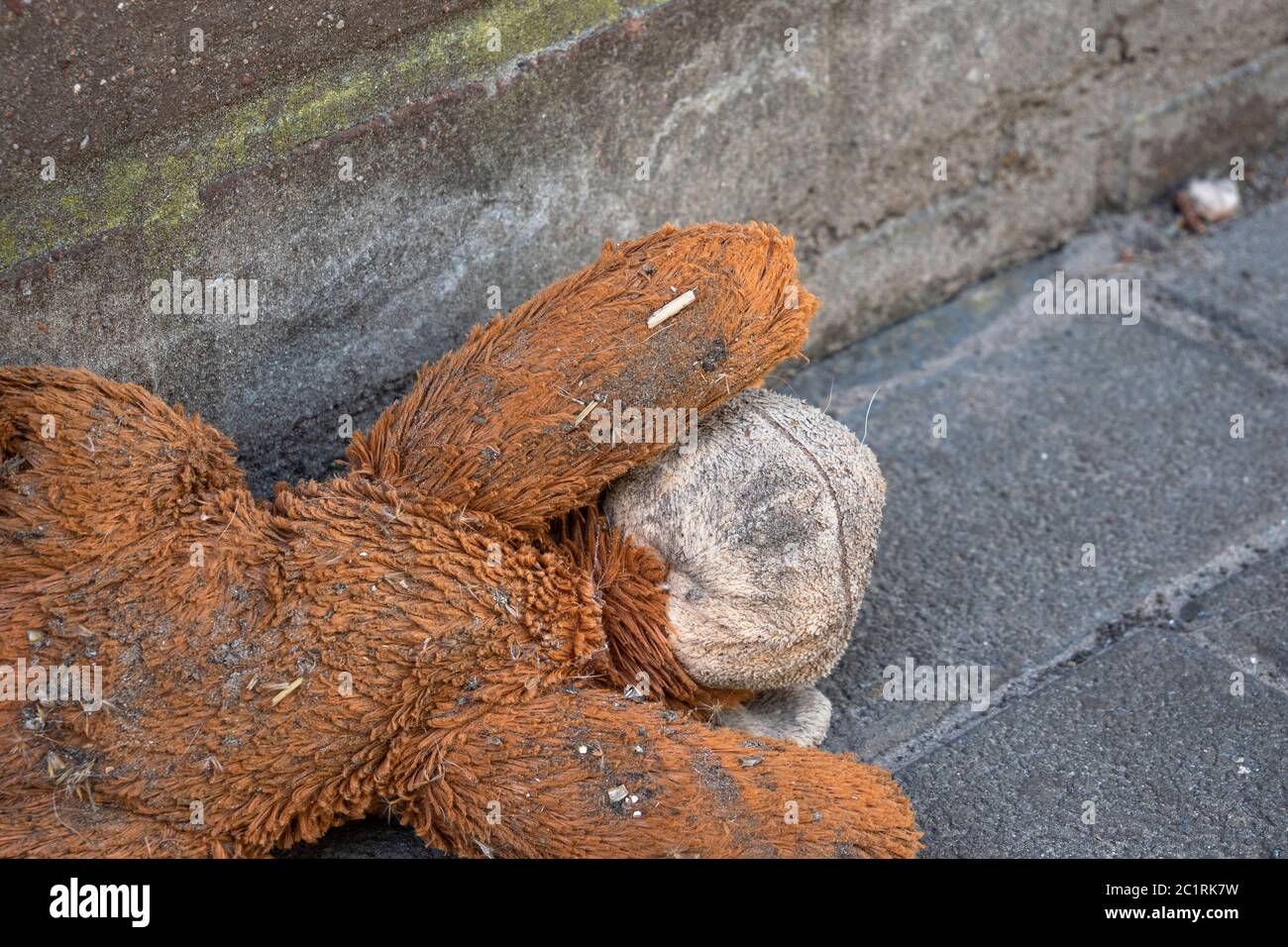 Old teddy bear is left in the dirt on the sidewalk Stock Photo