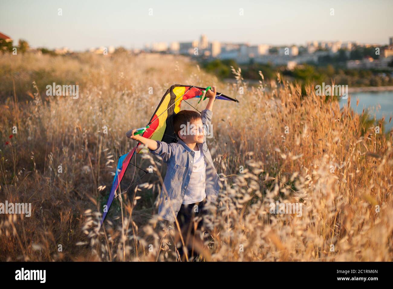 happy delightful smiling small kid with kite in hands standing on summer field nea sea port outside city Stock Photo