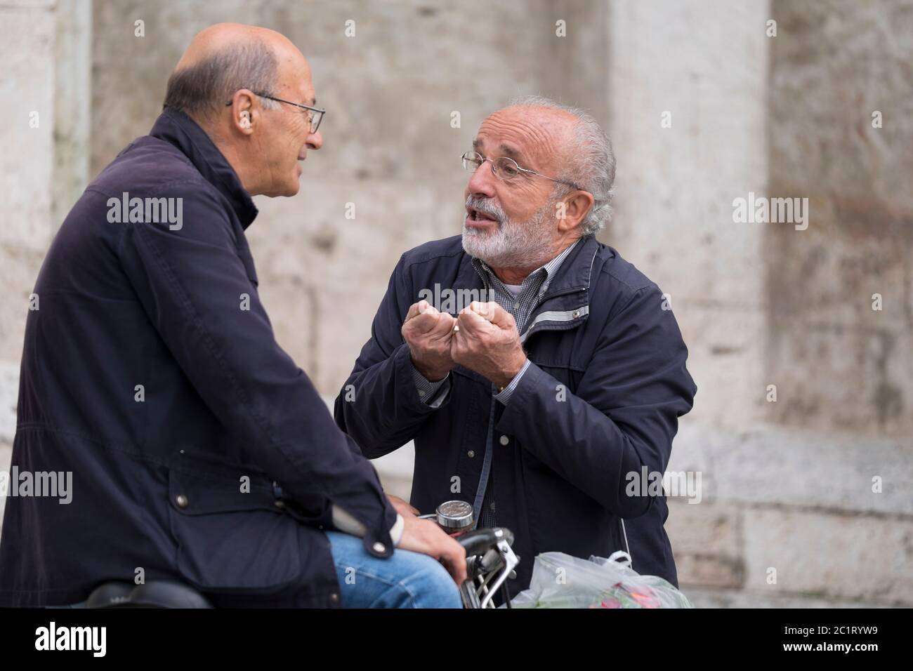 Two Italian men talk to each other and make typical Italian gestures on the square Piazza del Popolo in Ascoli Piceno, Italy Stock Photo