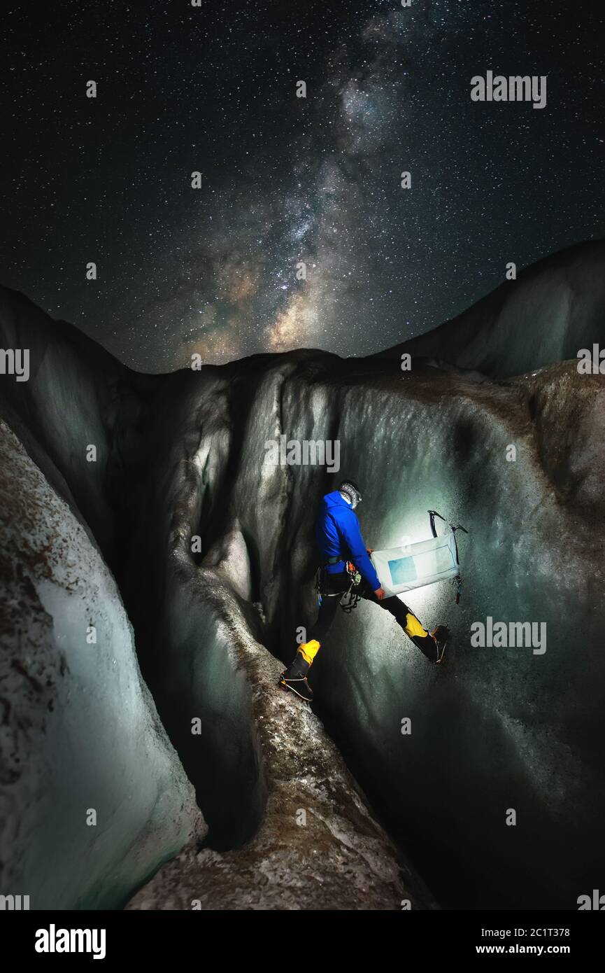 Night landscape of the glacier. male climber in a fissure with ice axes and an empty flag in his hands stands on an island betwe Stock Photo