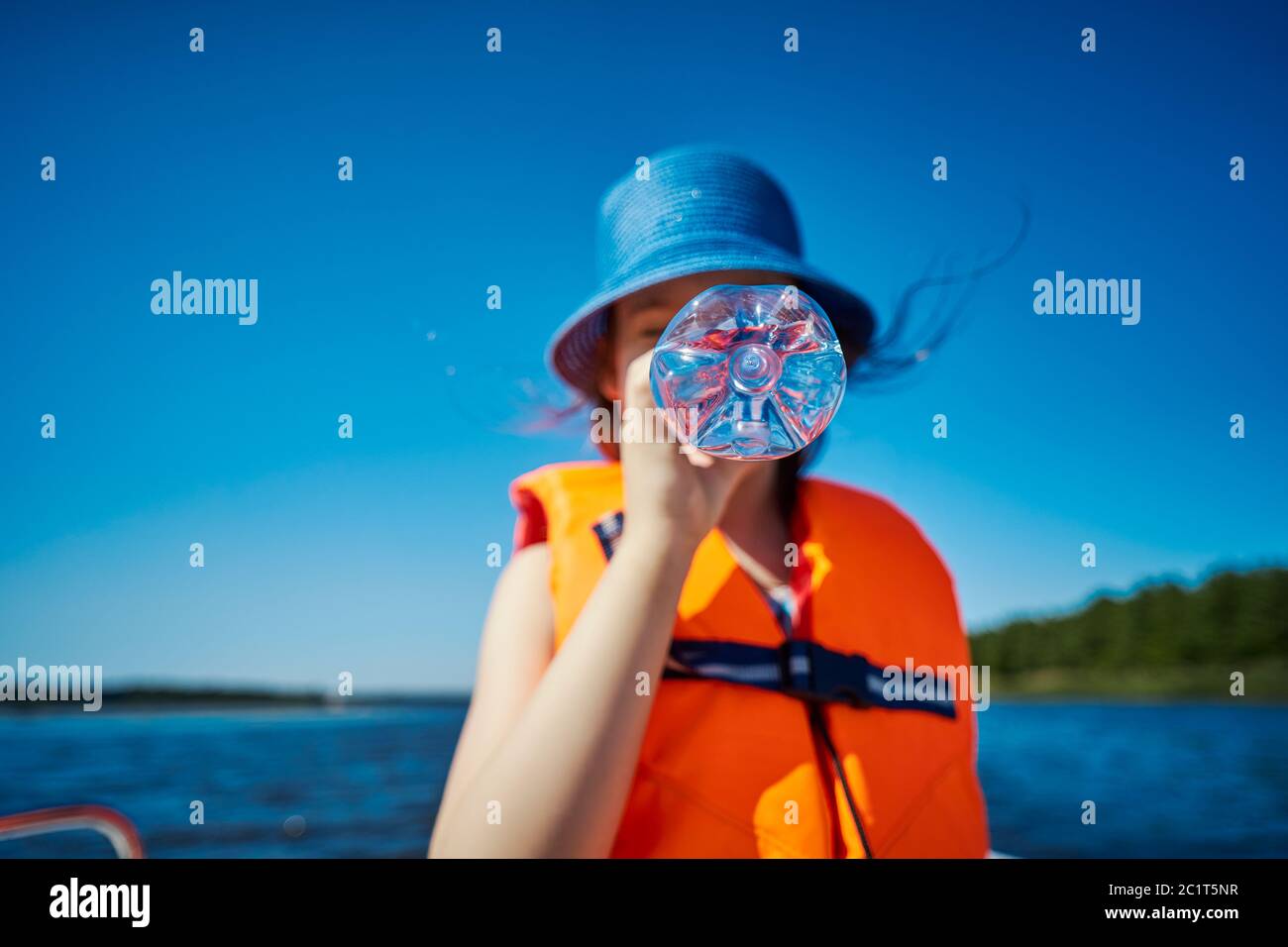 blurry little girl hides her mouth behind a bottle on a motorboat Stock Photo