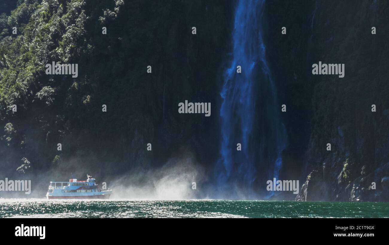 a cruise boat sails into the spray at the base of stirling falls in milford sound Stock Photo