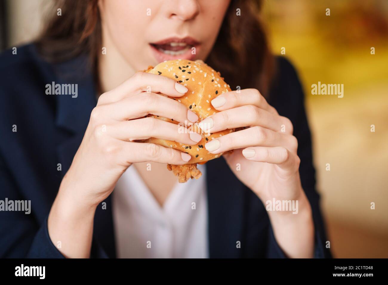 Female hands holding a burger near the mouth. Stock Photo