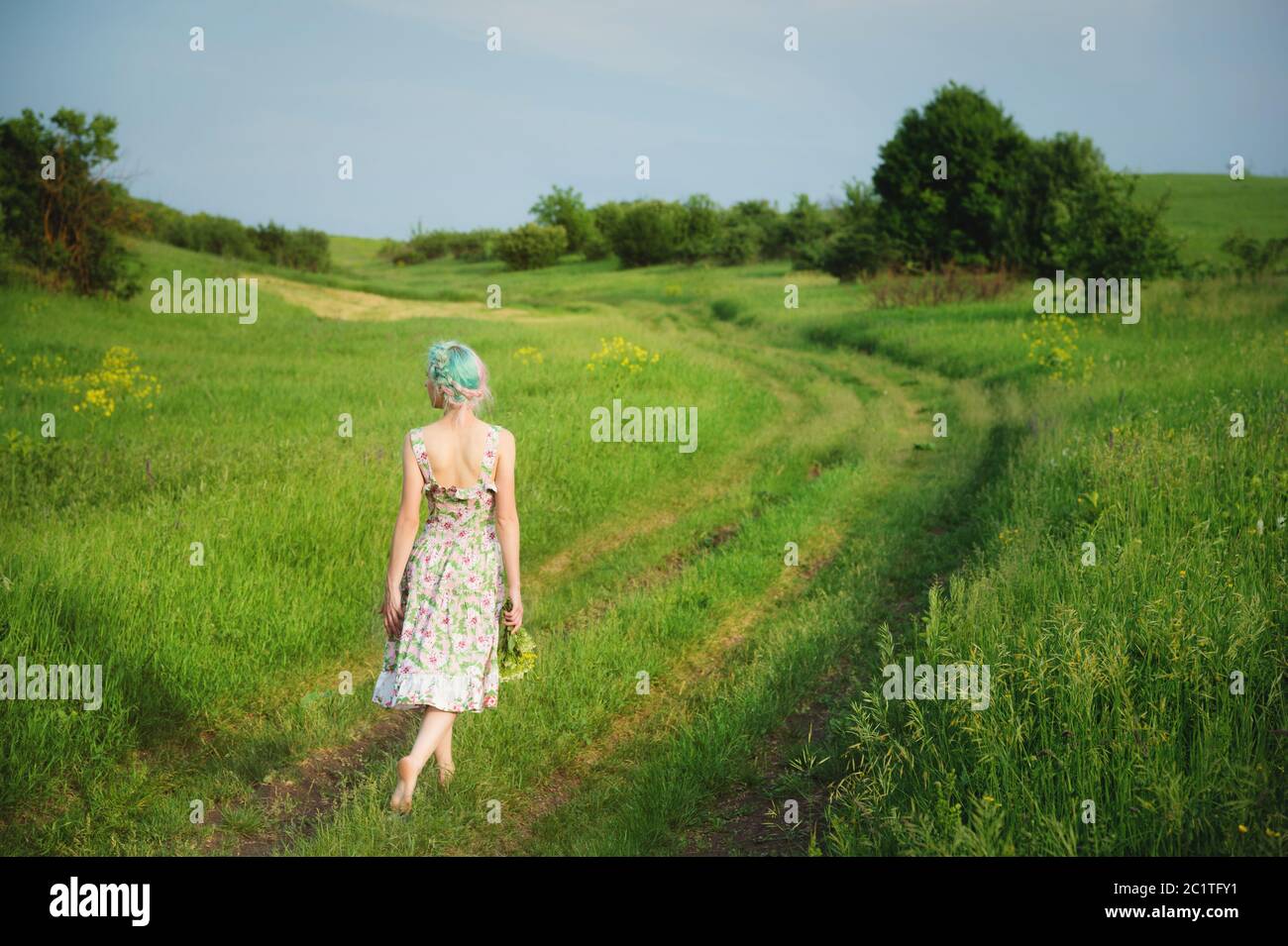 A cute cheerful young girl in a light cotton dress strolls along the ...