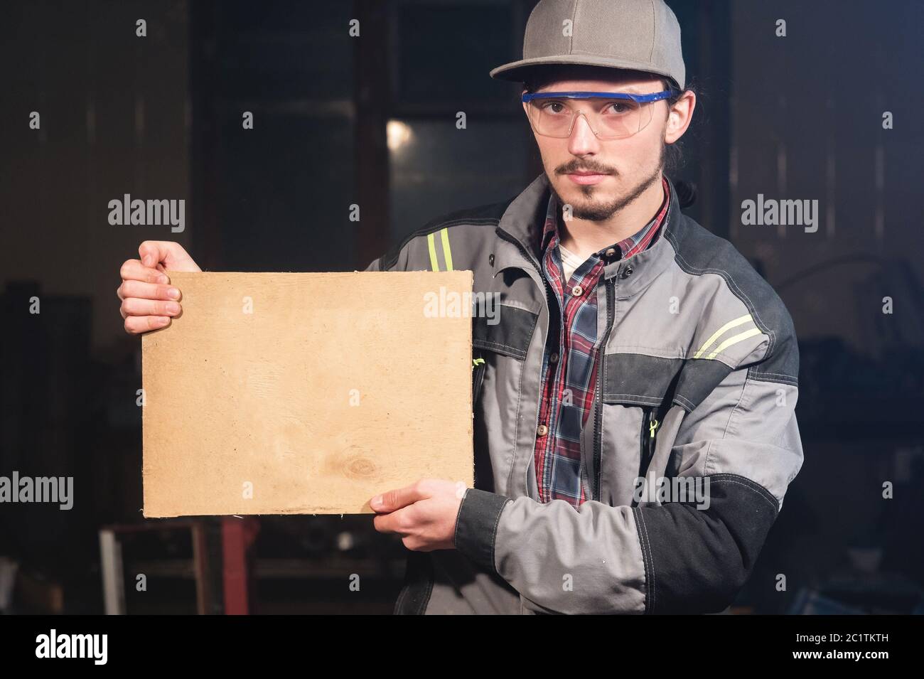 Portrait of a young carpenter in overalls and goggles with a mock up