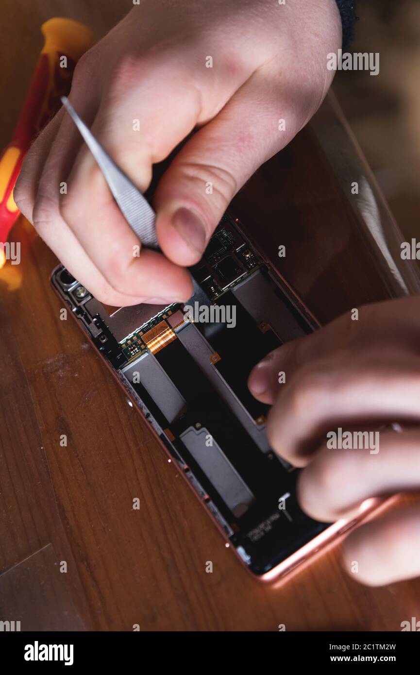 Close-up of the hand of a home craftsman repairing a disassembled smartphone. The concept of self-repair electronics at home Stock Photo