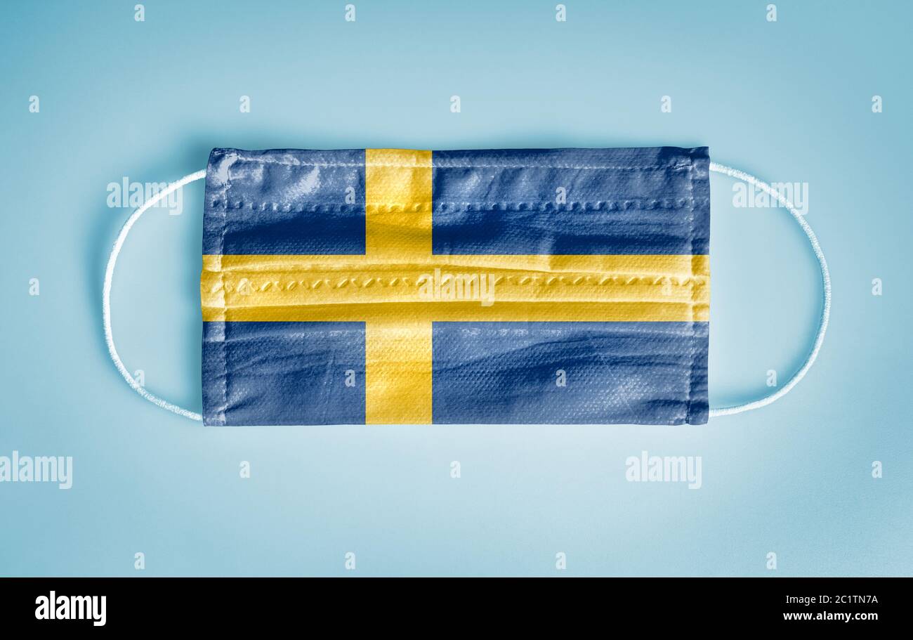 Covid-19 Coronavirus protection concept: Medical disposable face mask with Sweden flag on blue background.  WHO recommends usage of mask for preventio Stock Photo
