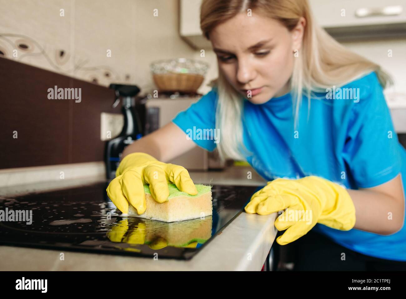 Woman, wearing in protective glove with rag, cleaning electric stove at home. Stock Photo