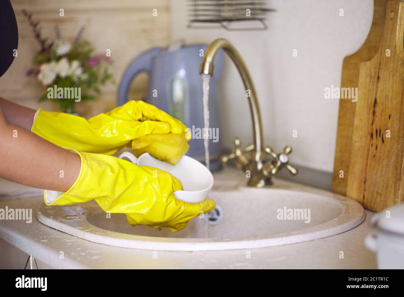 Close up hands of woman wearing yellow gloves washing dishes in kitchen