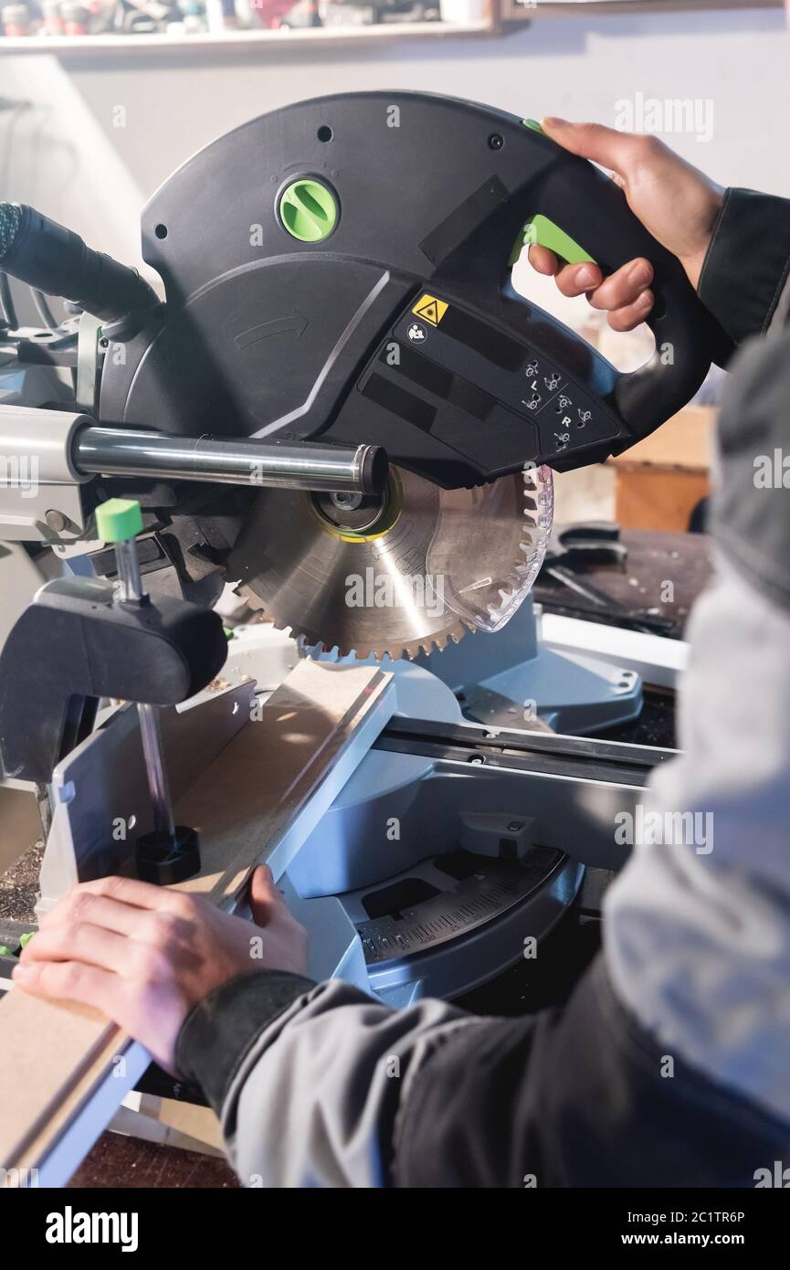 Close up of hands by profession a carpenter cuts wooden boards with a circular saw on a workbench table in a workshop. Professio Stock Photo