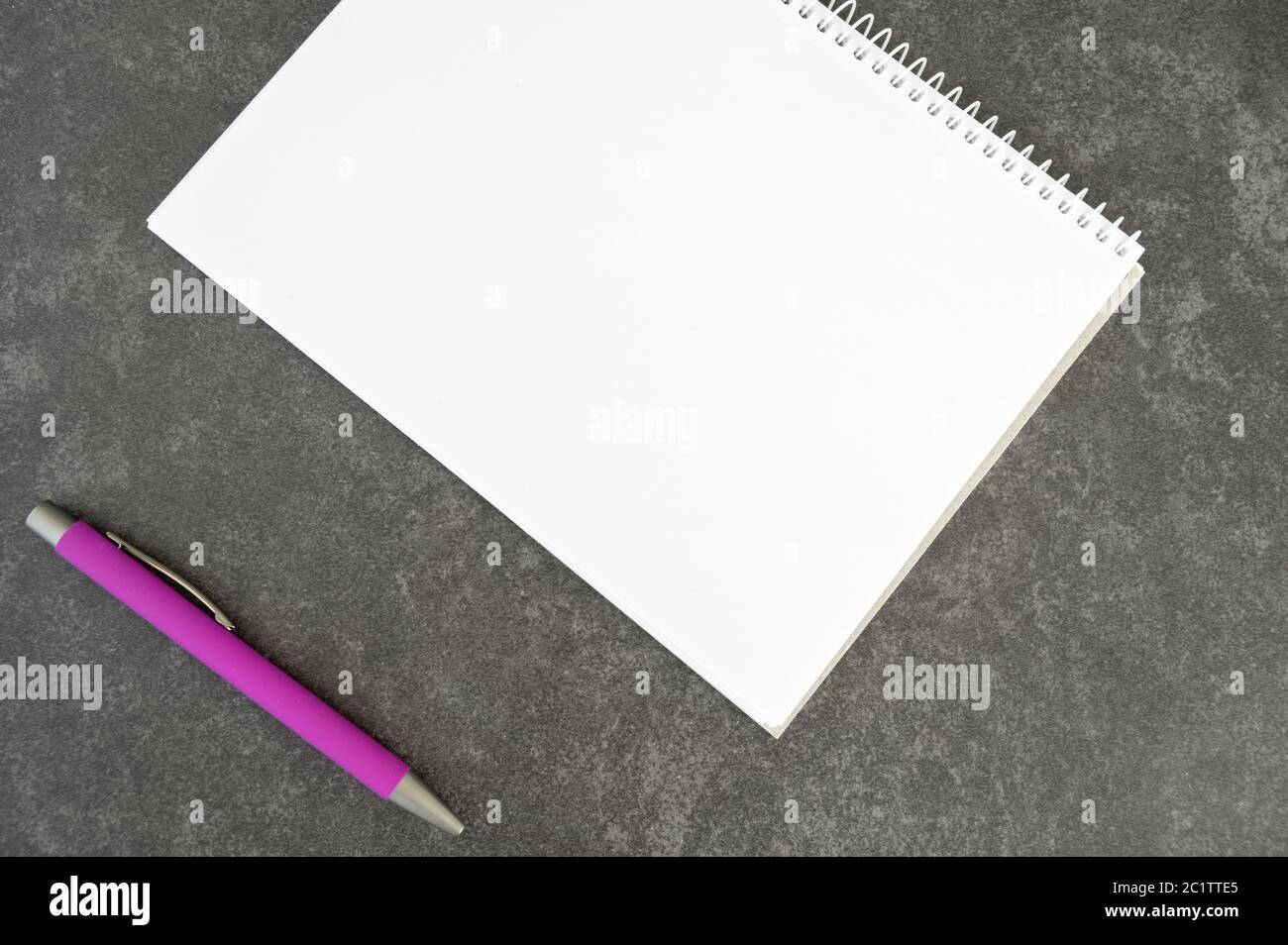 A blank notebook and a pink pen placed on textured stone table Stock Photo