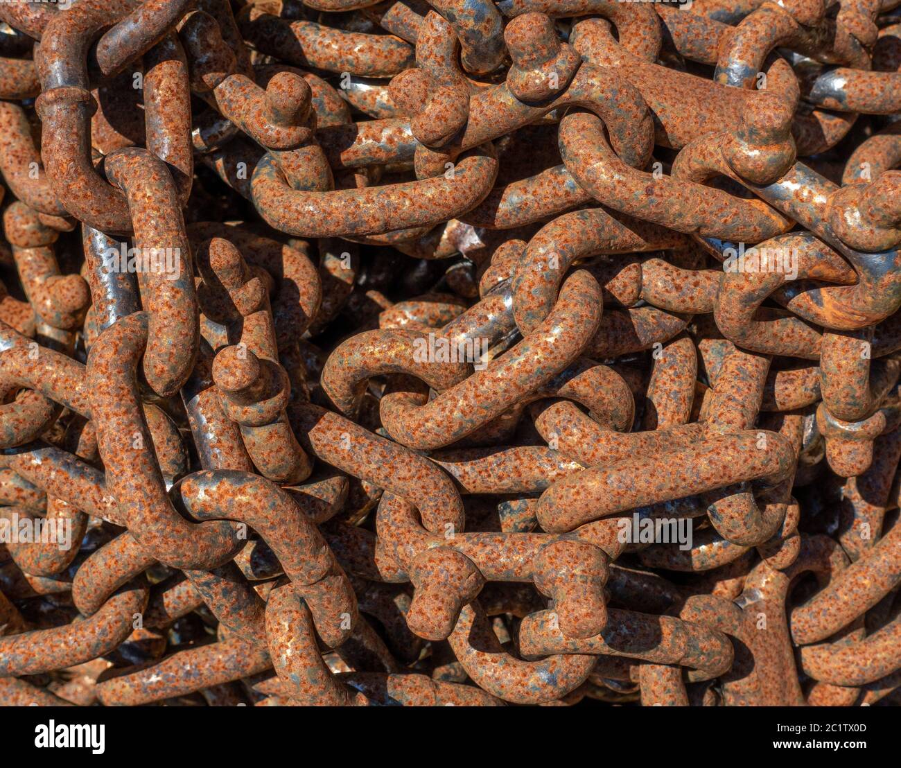 Rusty industrial chain with strong links in closeup lies disordered on top of each other in the sunshine Stock Photo