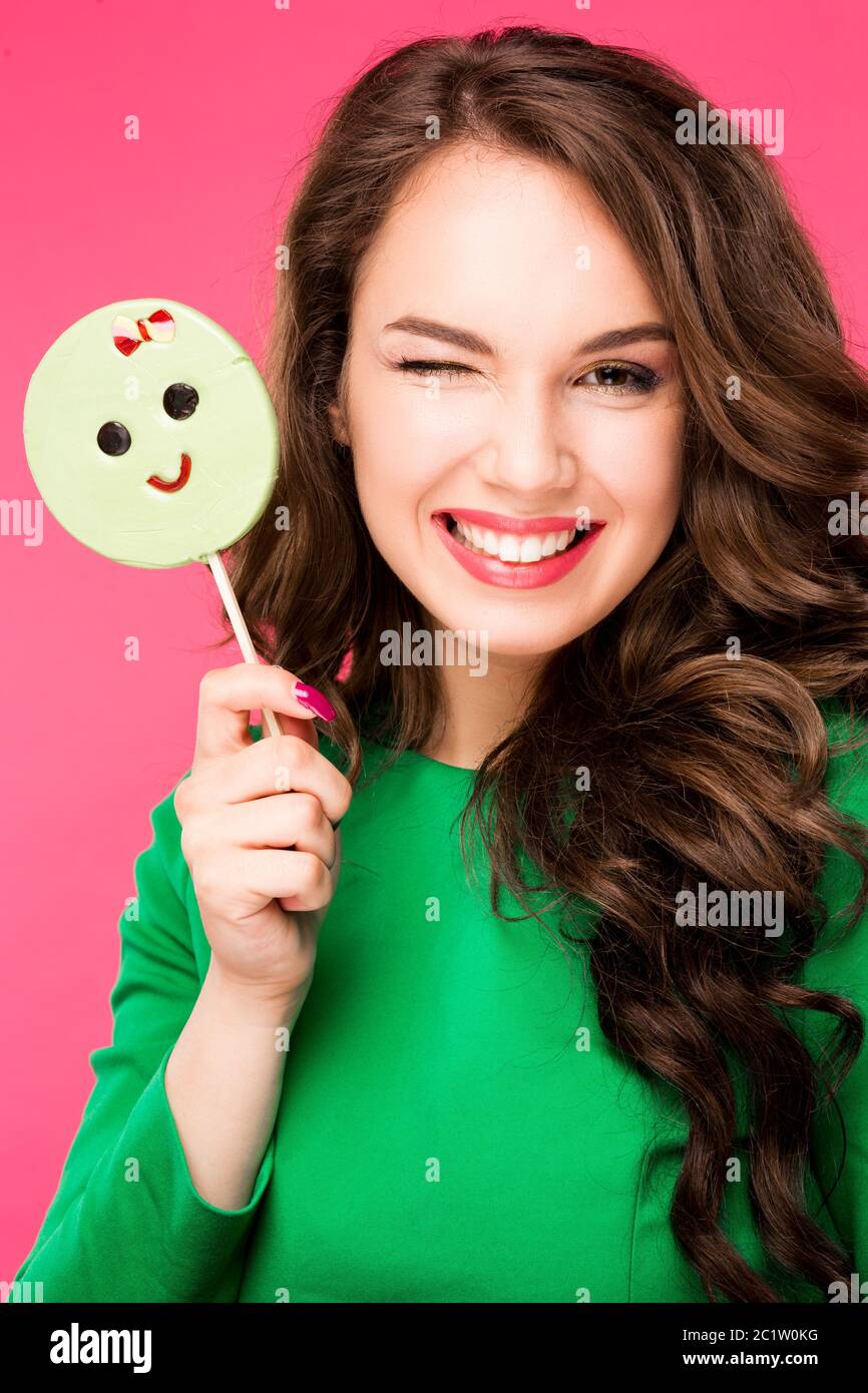 Beautiful young woman holds in hands candy smiling broadly. Stylish girl with bright makeup and  in her , isolated on pink backg Stock Photo
