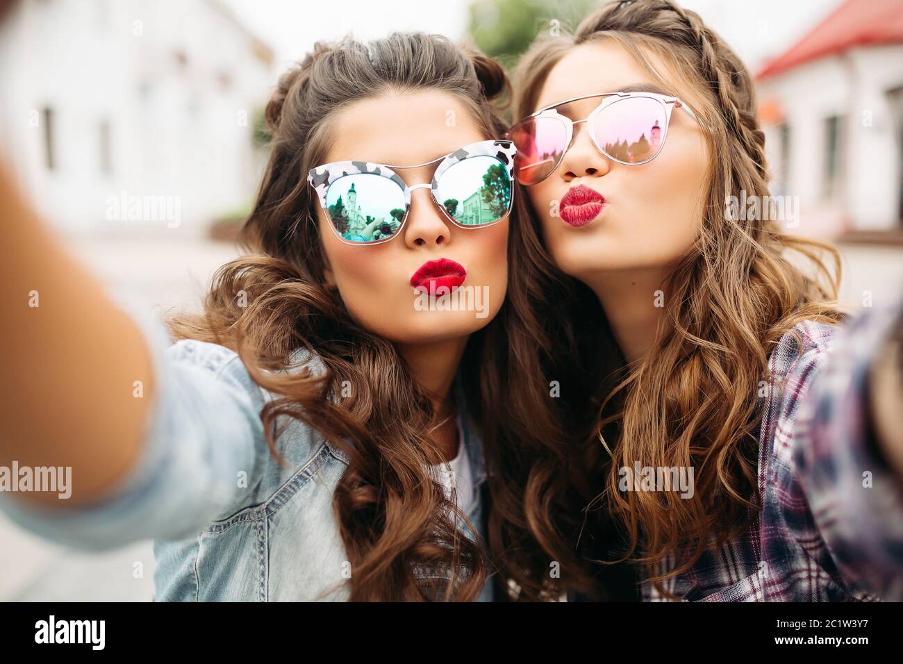 Gorgeous brunette girlfriends with hairstyle, mirrored sunglasses and red lips making selfie with duck face. Stock Photo