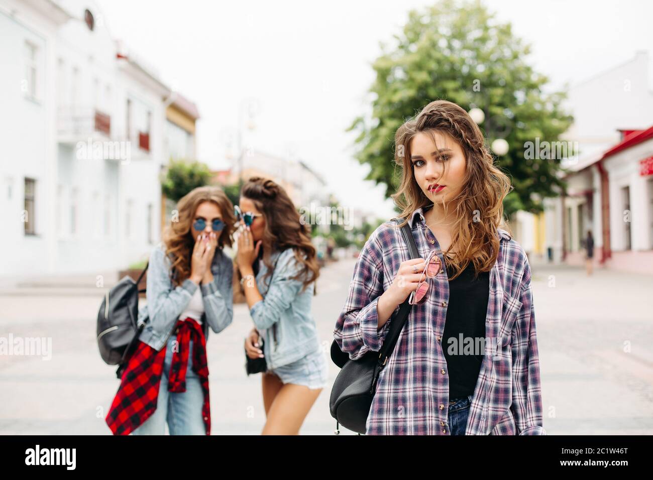 Jealous girls whispering about third girl in front of camera. Stock Photo