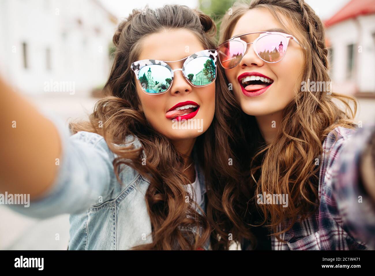 Gorgeous brunette girlfriends with hairstyle, mirrored sunglasses and red lips making selfie with duck face. Stock Photo