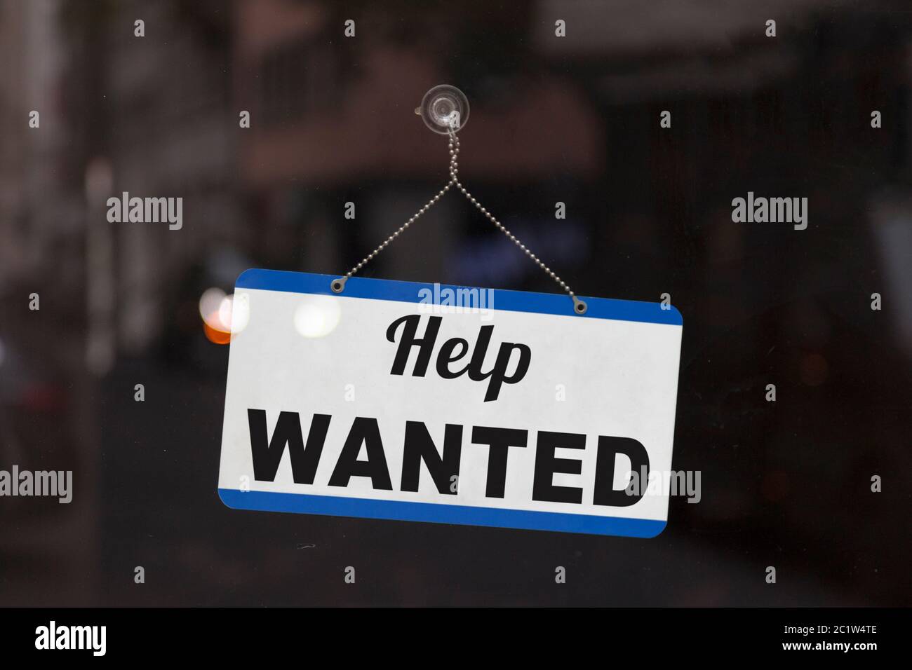 Close-up on a blue open sign in the window of a shop displaying the message 'Help wanted'. Stock Photo