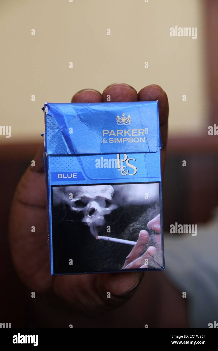 Hand holding Parker & Simpson cigarette packet with warning label picture, Andoany/Hell-Ville City, Nosy Be, Madagascar. Stock Photo