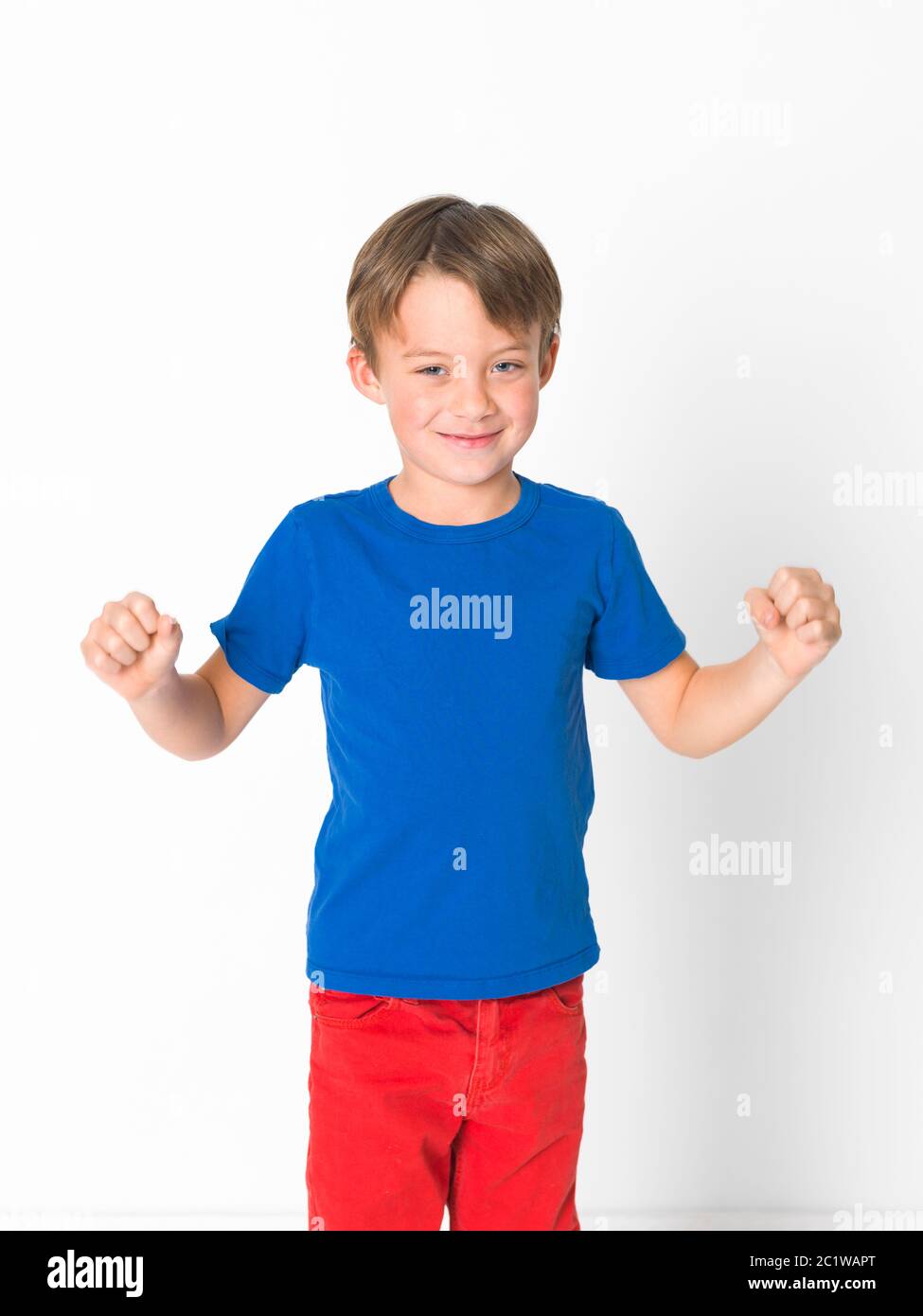 cool and cute six year old boy in red trousers and blue shirt is posing in front of white background Stock Photo