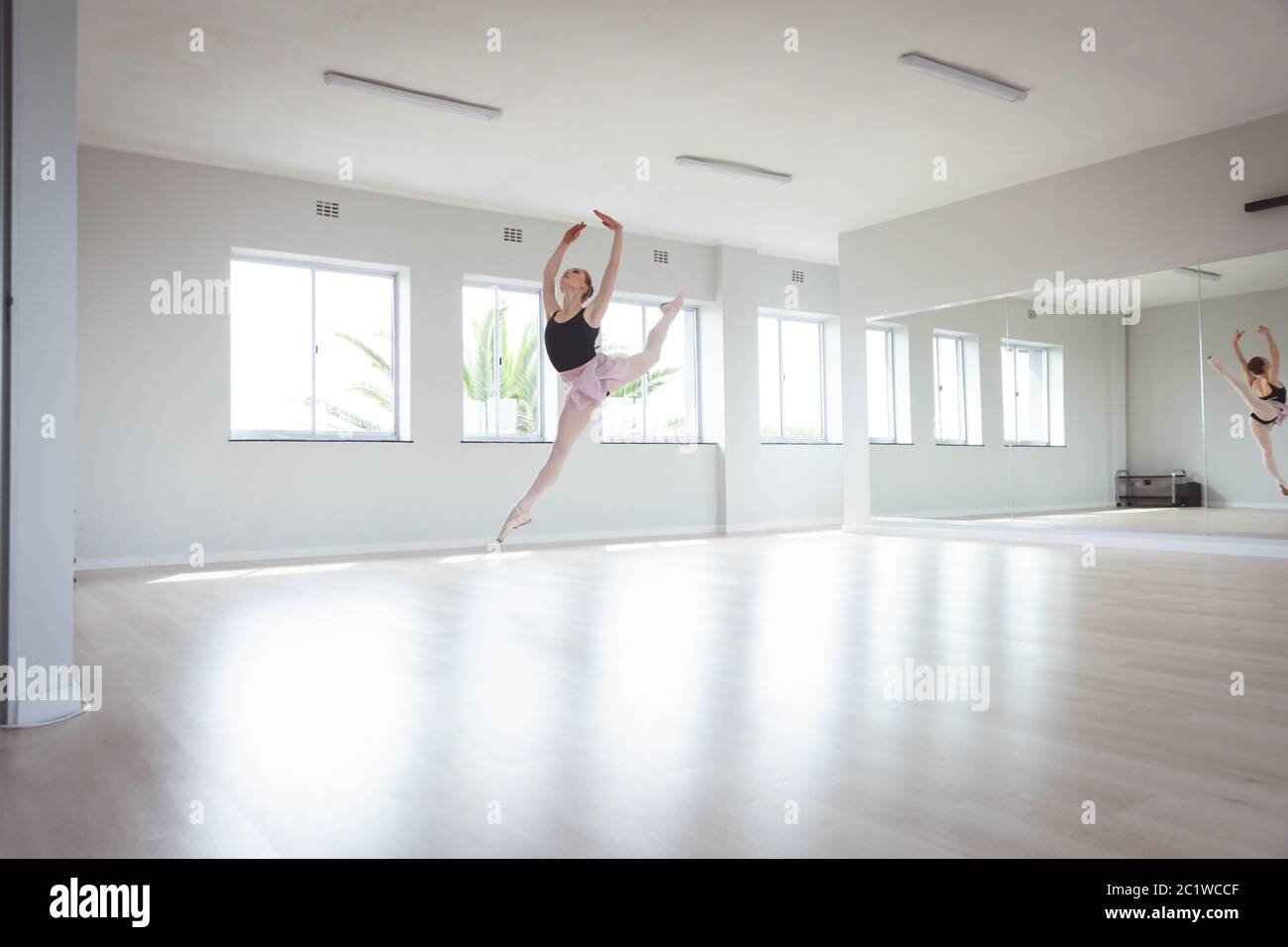 Caucasian female ballet dancer jumping in the air with her arms above her head Stock Photo
