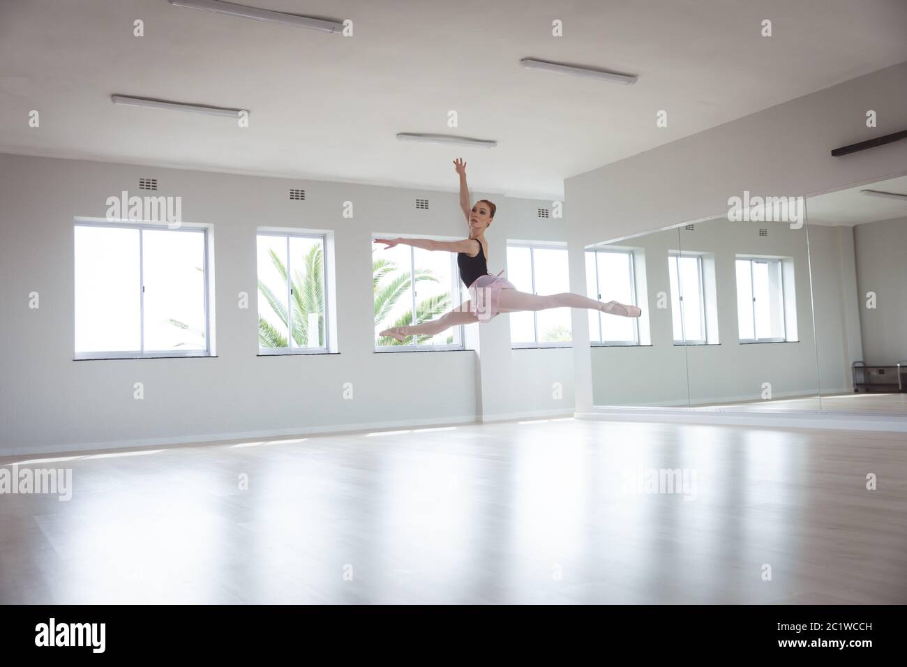 Caucasian female ballet dancer jumping in the air with her arms above her head Stock Photo