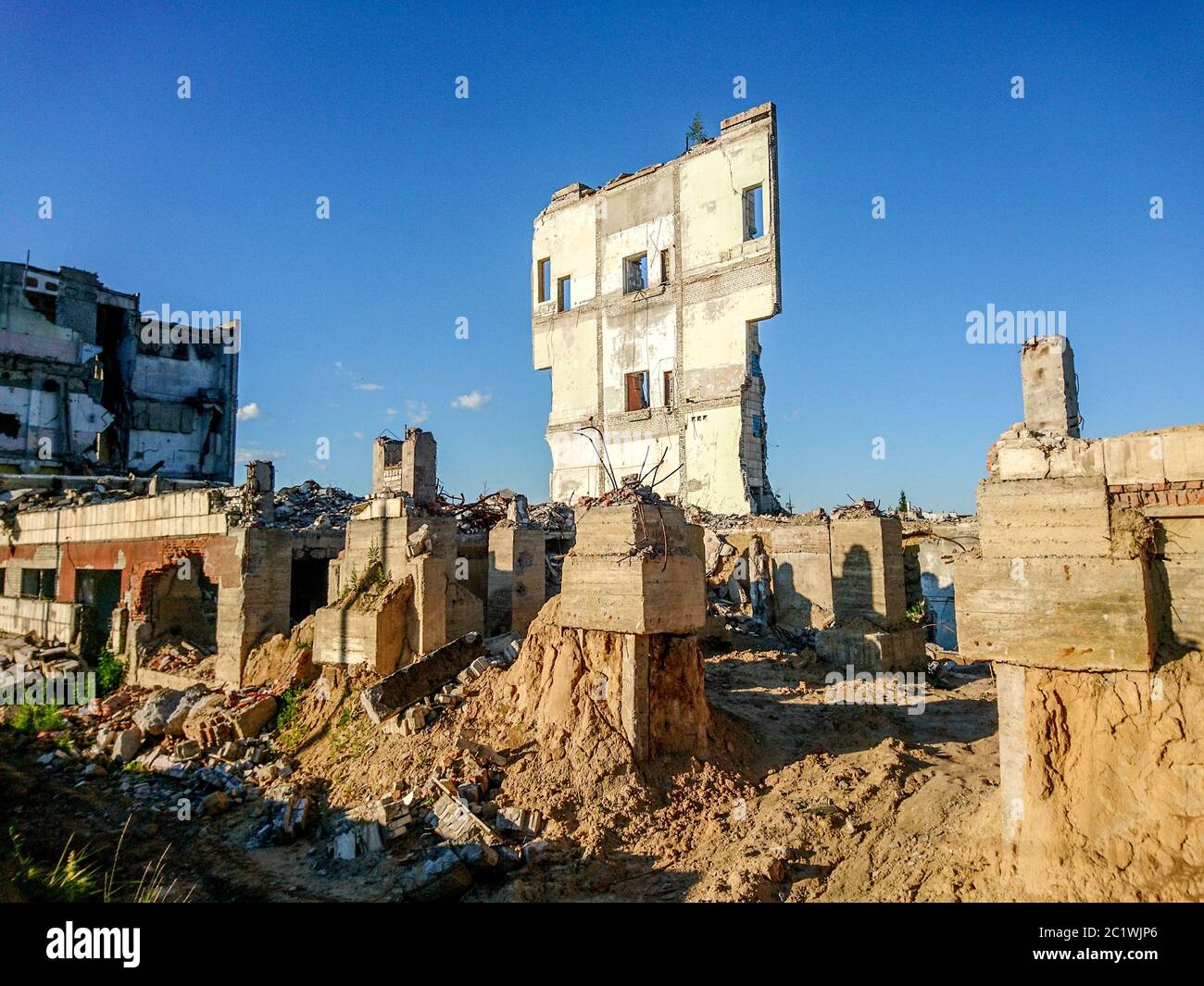 The ruins of a large destroyed building, pieces of stone, concrete, clay and metal against the blue Stock Photo