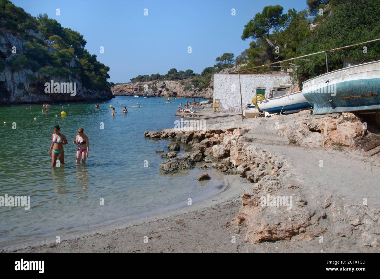 Tourists wading and bathing in the cove at Cala Pi near old boat houses, Mallorca south coast, August. Stock Photo