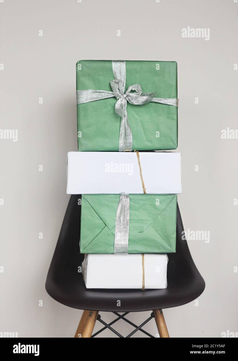 Green and white Christmas gift boxes with red ribbons on chair by the grey wall Stock Photo