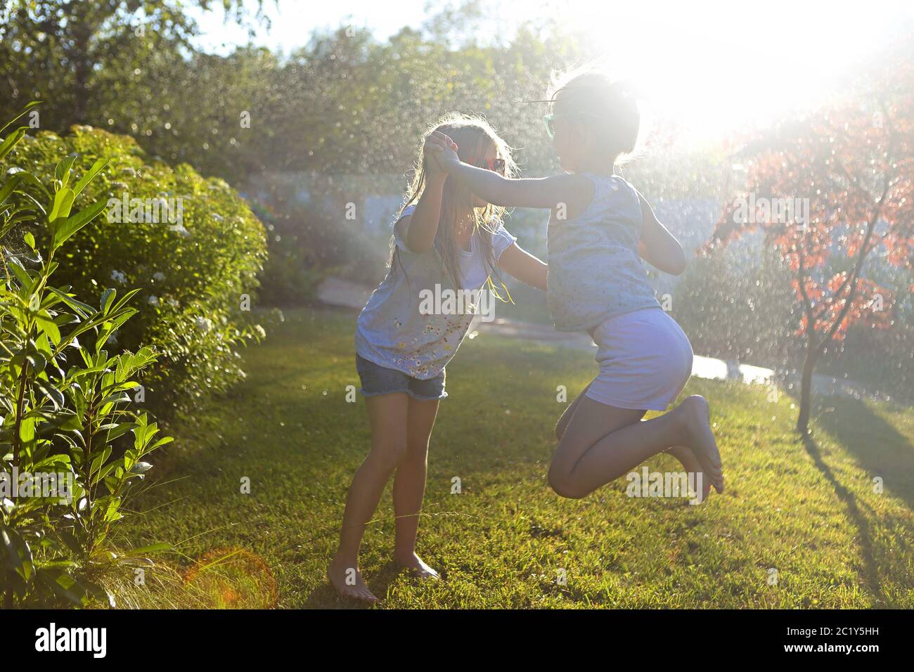 Child playing with garden sprinkler. Kids run and jump. Summer outdoor water fun in the backyard. Children play with hose wateri Stock Photo