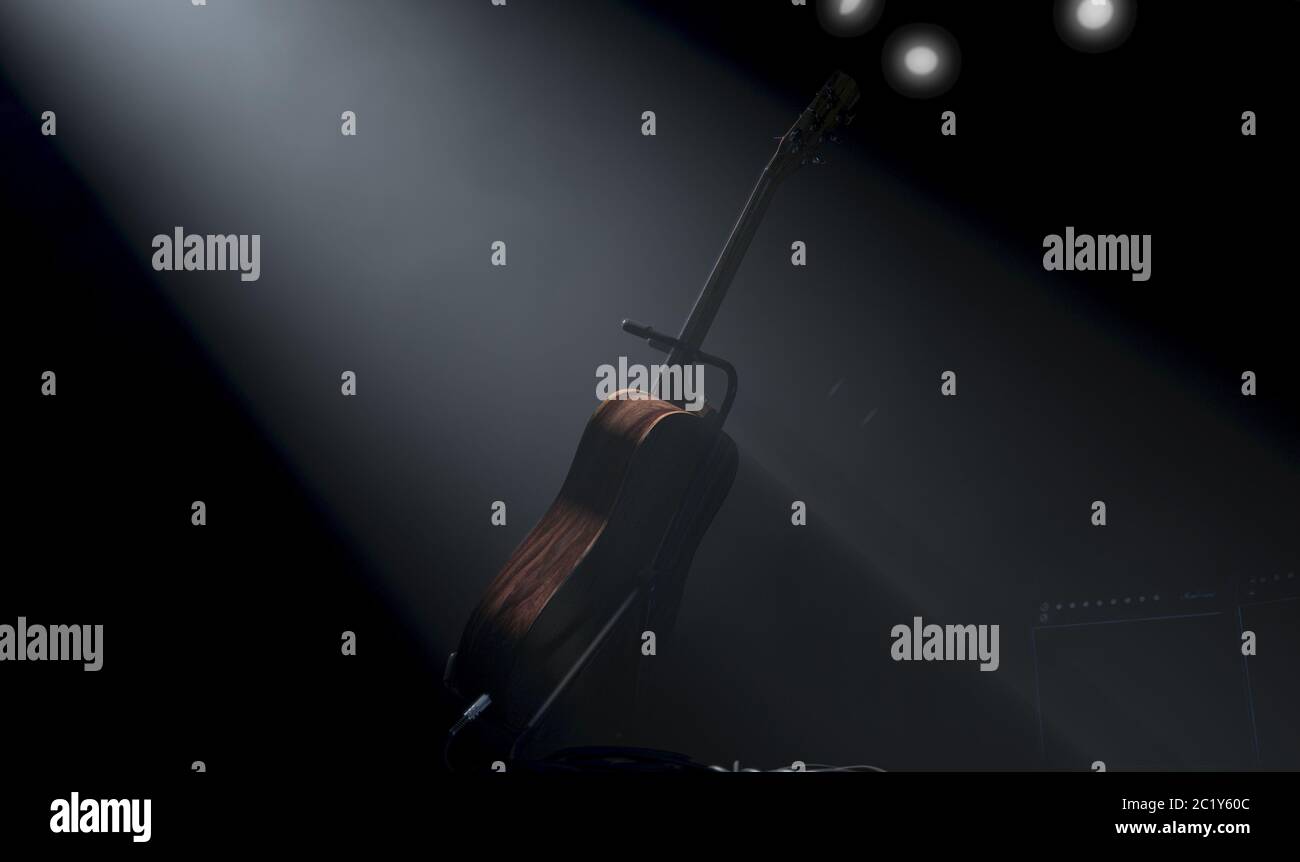 An acoustic guitar resting on a stand on a music concert stage lit by a single dramatic spotlight on a dark background - 3D render Stock Photo