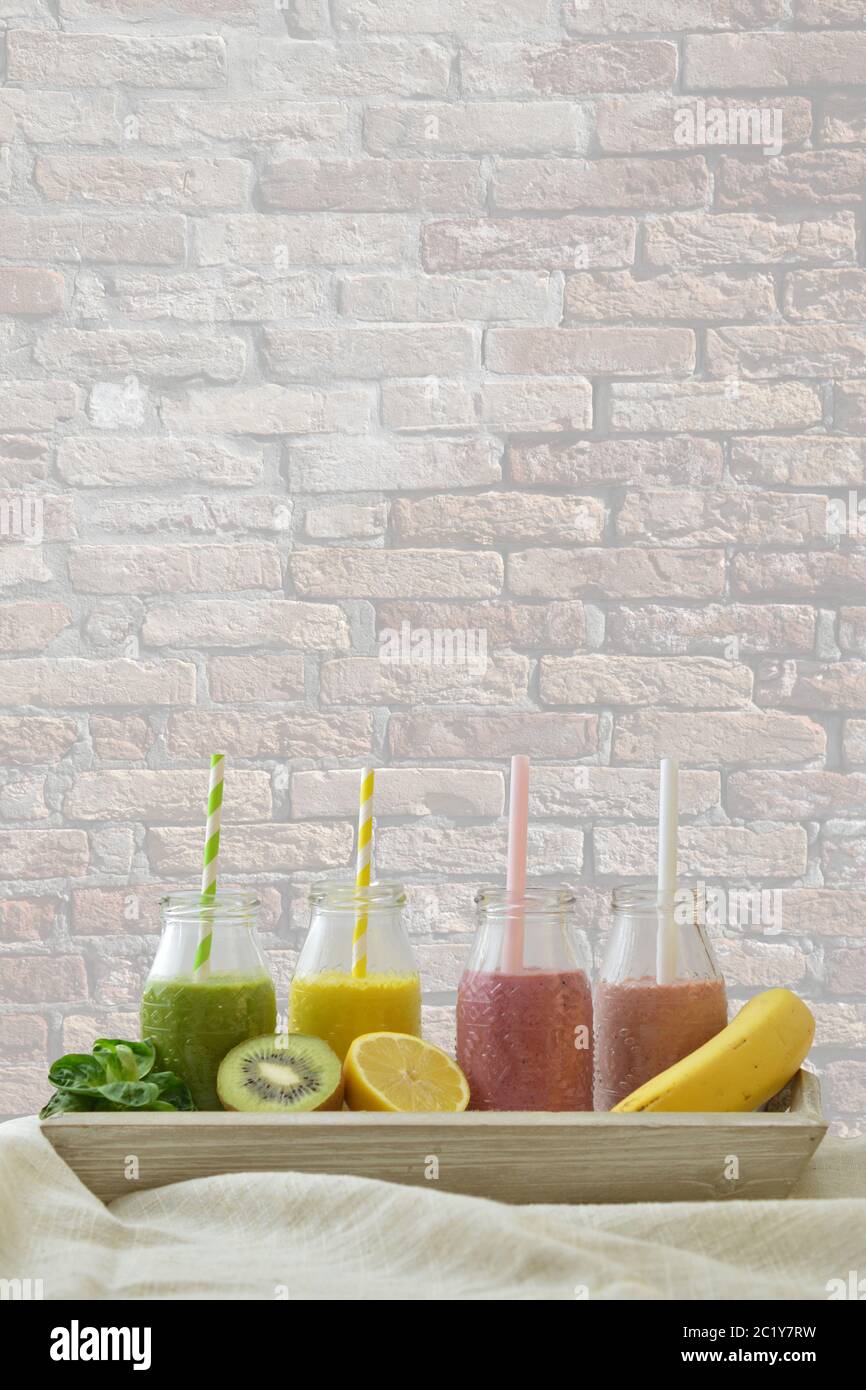 colorful fruit smoothies in a row with fresh fruits in front of a wall Stock Photo